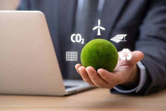 A businessman is holding a green sphere with icons of renewable energy sources, representing the concept of environmental responsibility, sustainable development, and corporate social responsibility f