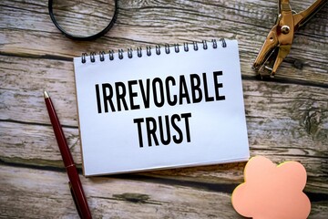 IRREVOCABLE TRUST written on a notebook. A beautiful wooden table. A pen, a nice decorative...