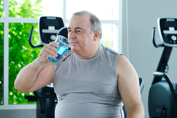 A man takes a break to drink water after exercising at the gym as part of his weight loss workout.