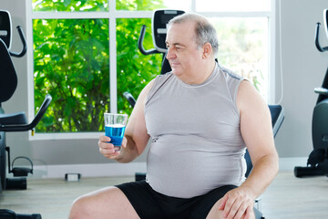 A man takes a break to drink water after exercising at the gym as part of his weight loss workout.