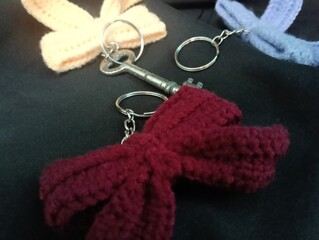 Three handmade crochet keychains and a key featuring bow designs in pastel colors lie on a black...