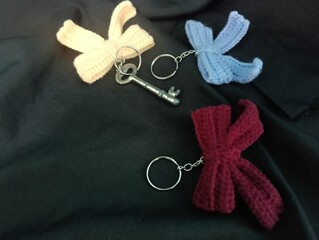 Three handmade crochet keychains and a key featuring bow designs in pastel colors lie on a black fabric. photo taken in malaysia