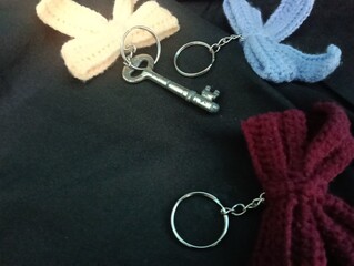 Three handmade crochet keychains and a key featuring bow designs in pastel colors lie on a black fabric. photo taken in malaysia