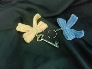 Three handmade crochet keychains and a key featuring bow designs in pastel colors lie on a black...