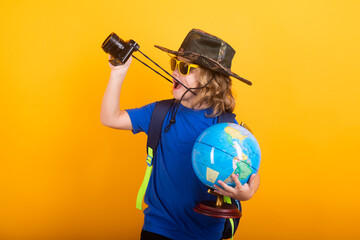 Kid tourists with backpacks and camera hold world globe isolated on yellow studio background. Child boy with backpacks exploring world and environment. Leisure activity for children.