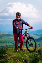 Unrecognizable athlete in protective gear standing in a field and looking at the camera against the backdrop of foggy mountains and cumulus clouds. Mountain sports concept