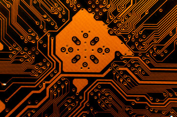 Orange computer circuit parts in neon light. Macro photo of a board painted in red tones