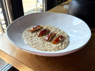 Creamy risotto with eel served in plate. Modern cuisine concept. Handheld mobile photo, selective...