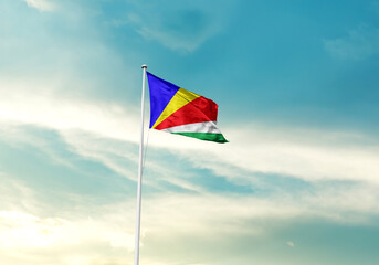 Seychelles flag is waving on a tall flagpole among the clouds. Seychelles national flag for independence day.