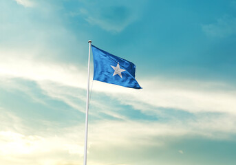 Somalia flag is waving on a tall flagpole among the clouds. Somalia national flag for independence day.