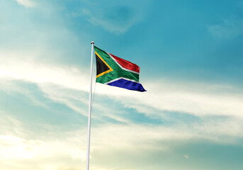 South Africa flag is waving on a tall flagpole among the clouds. South Africa national flag for independence day.