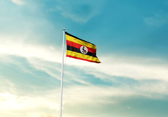 Uganda flag is waving on a tall flagpole among the clouds. Uganda national flag for independence day.