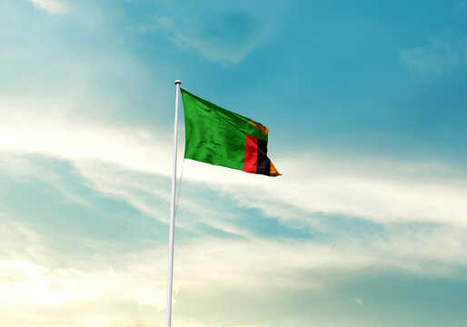 Zambia flag is waving on a tall flagpole among the clouds. Zambia national flag for independence day.