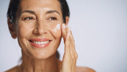 Radiant mature woman with a joyful smile applying nourishing face cream.