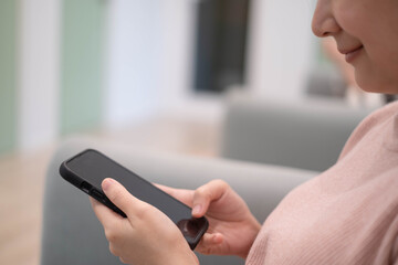 A woman interacts with her smartphone while seated, focusing on the screen in a cozy indoor...
