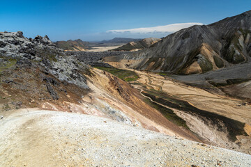 Blick vom Berg Brennisteinsalda in Landamannalaugar auf island nach unten, im Hintergrund Lavafeld unter blauem Himmel, im Vordergrund bunte Berge und moosbewachsene Lava