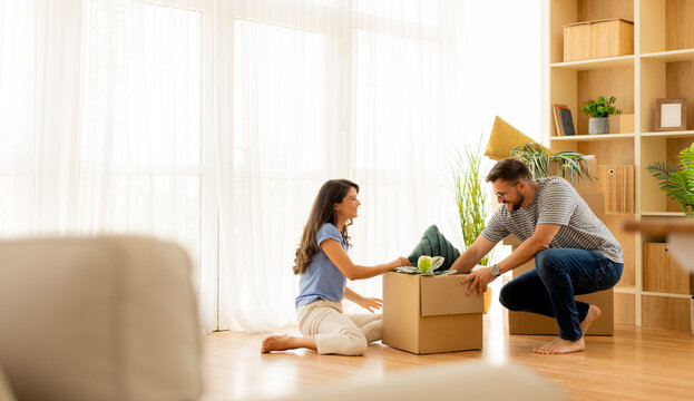Couple unpacking boxes in a bright living room during a sunny afternoon