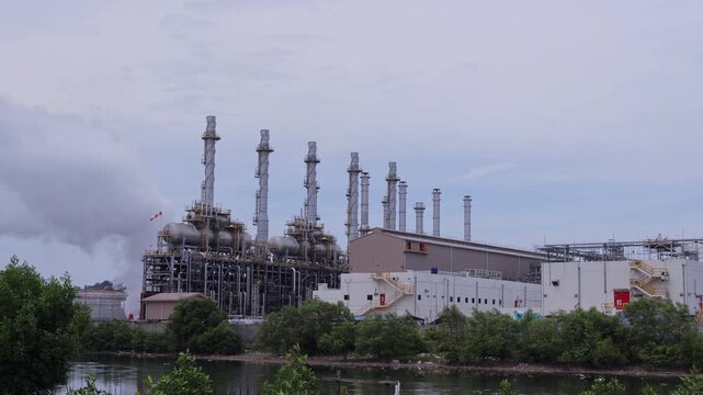 Pertamina Oil and gas refinery industry, equipment details Steel oil pipelines with valves from large oil storage tanks and mangrove conservation as foreground.