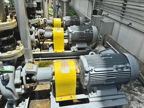 industrial machine in the factory Three large industrial electric motors connected to pumps and pipes in a factory or plant. The robust machinery and bright yellow protective guards highlight a powerf