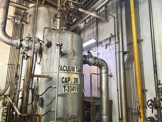 A weathered vacuum tank with intricate pipes and gauges in a power plant or industrial facility....