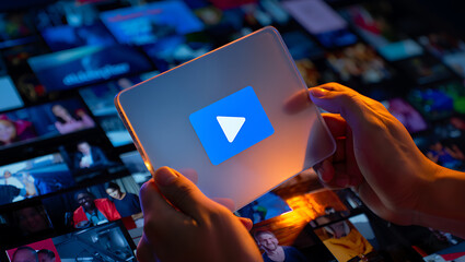 Hands holding transparent device with play button over media wall image