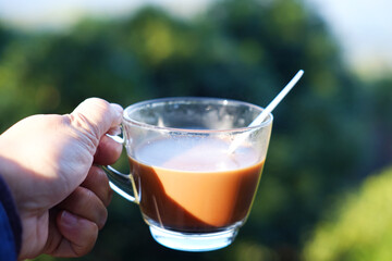 Close up hand holding a glass cup of hot coffee on the valley mountain in natural sunlight of morning bright day
