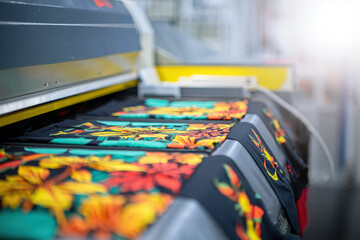 Close up view of a modern textile printing machine with colorful patterned shirts on the conveyor belt