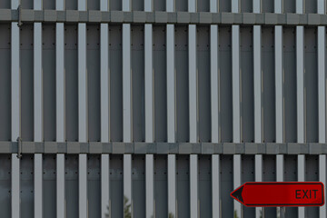 There is a fence in place, and right in front of it, there is a bright red exit sign that is easily visible to anyone nearby