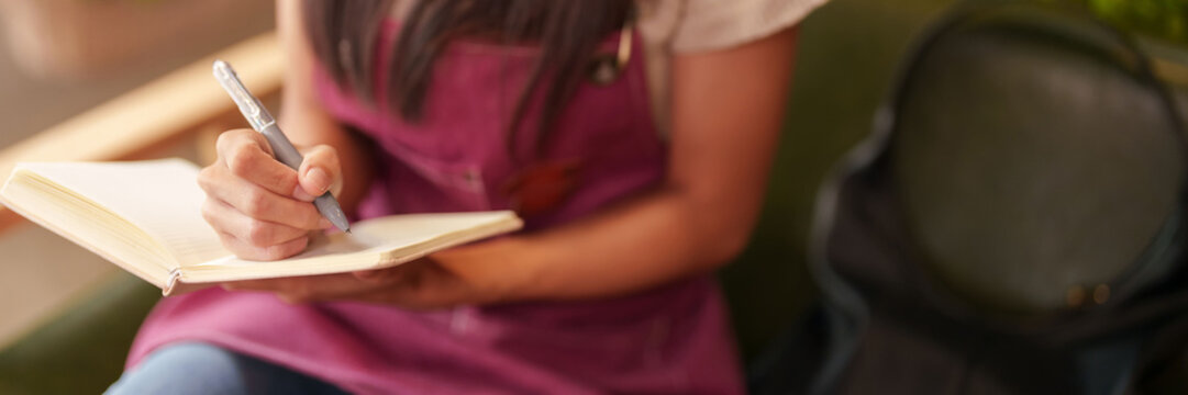 Asian adult woman working flower shop writing notes planning floral business growth managing daily operations efficiently