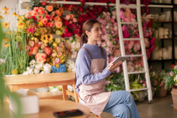 Asian adult florist manages flower shop operations Small business woman organizes floral orders digital tablet vibrant bloom store