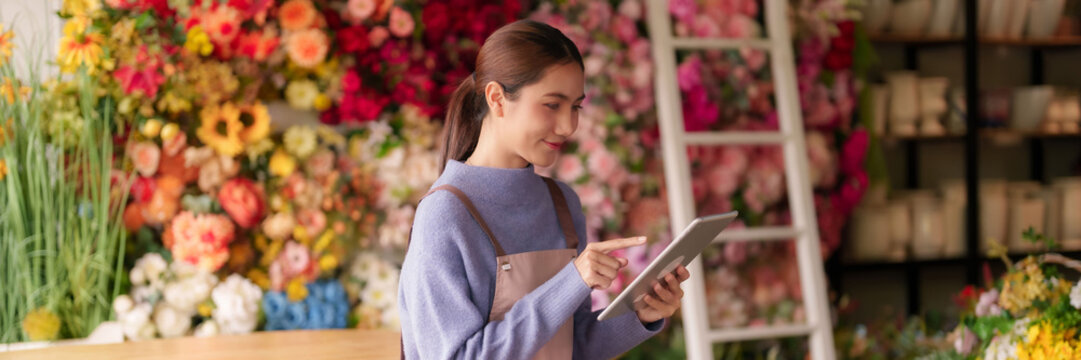 Asian adult woman florist small business owner manages orders inventory customers using digital tablet vibrant colorful flower shop boutique for efficient retail operations - Powered by Adobe