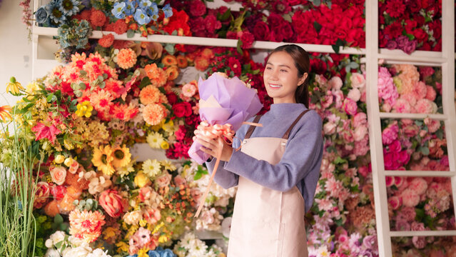 Asian adult woman florist prepares beautiful vibrant flower arrangements in colorful flower shop displaying fresh blossoms