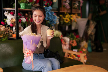 Smiling Asian adult woman customer holds fresh flowers coffee enjoys purchase beautiful flower shop