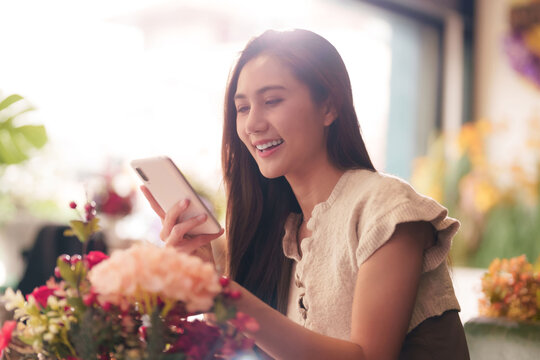 Asian adult woman smiles uses smartphone flower shop browsing flowers happy customer florist online shopping
