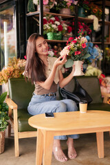 Asian adult woman happy admires flower arrangement cozy flower shop cafe purchases beautiful floral...