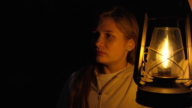 A lonely, anxious woman at night with a burning lamp in her hand. The concept of anxiety, arousal and fear.