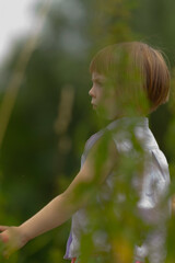 In a vast and vibrant field full of lush greenery, a little girl is joyfully standing with her arms...