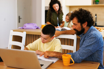 Father helping son with homework in kitchen while mother supervises daughter