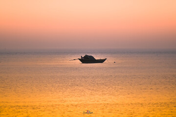 A small traditional fishing boat floats on a calm sea under a vibrant sunrise sky.
