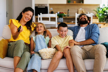 Happy family watching tv and laughing together at home