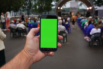 Man holding smartphone with green screen at outdoor music festival