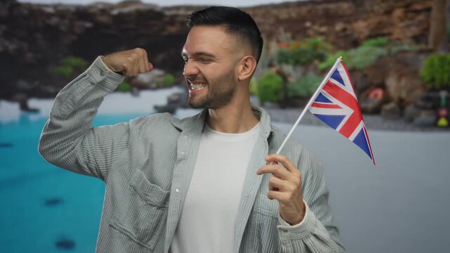 Hispanic man in a hotel swimming pool confidently flexing his arm while holding a uk flag, symbolizing joy and patriotism.