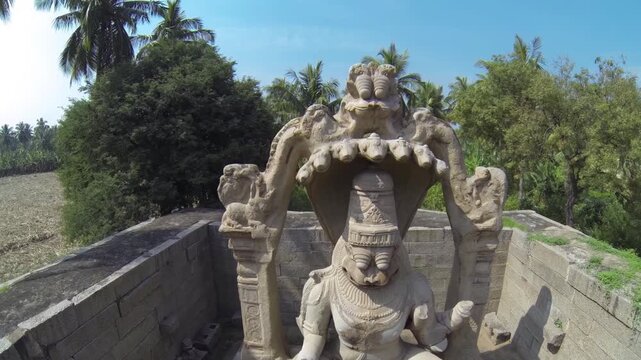 Drone footage flying towards majestic Narasimha statue in Hampi, then rising to reveal vast banana plantations. Captures Karnataka's spiritual and agricultural beauty.