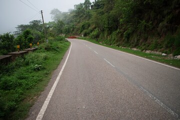 A winding empty road curving through lush green hills and dense forest under soft natural light, ideal for travel and nature themes.