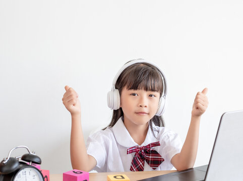 A Chinese elementary school girl is taking online classes at her desk. 