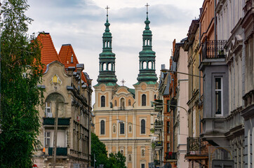 Obraz premium View of a baroque church with twin towers in the center of Poznań, framed by historic tenement buildings.