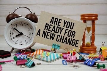 Are You Ready For A New Change? text on paper card with alarm clock and stationary on wooden...