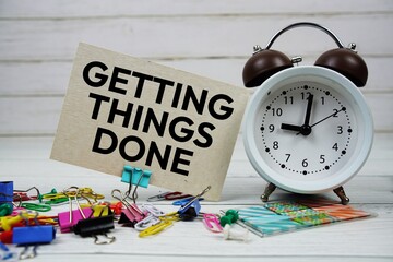 Getting Things Done text on paper card with alarm clock and stationary on wooden background