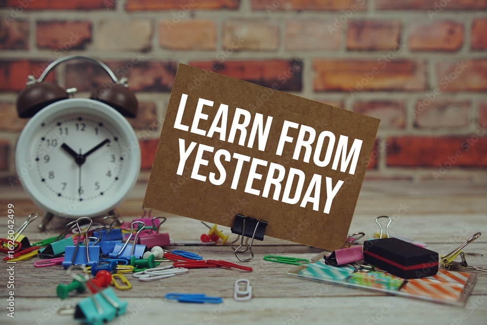 Poster learn from yesterday text on paper card with alarm clock and stationary on wooden background