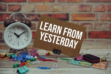 Learn from Yesterday text on paper card with alarm clock and stationary on wooden background